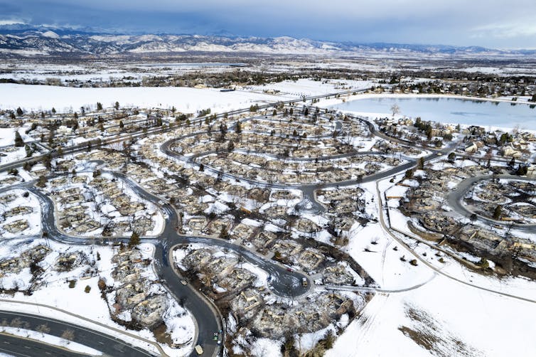 An aerial view of burned neighborhoods with a few houses standing among burned lots and at the edges of the fire area.