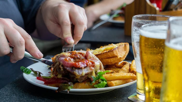 A person uses a fork and knife to cut their hamburger in half.