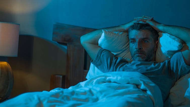 A man lies awake in bed looking pensive.