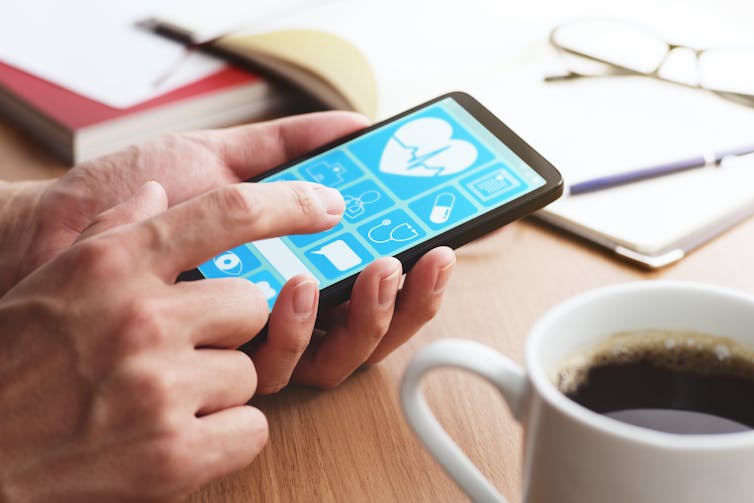 A white person's hands holding a smartphone with screen showing a health app, next to a cup of coffee.