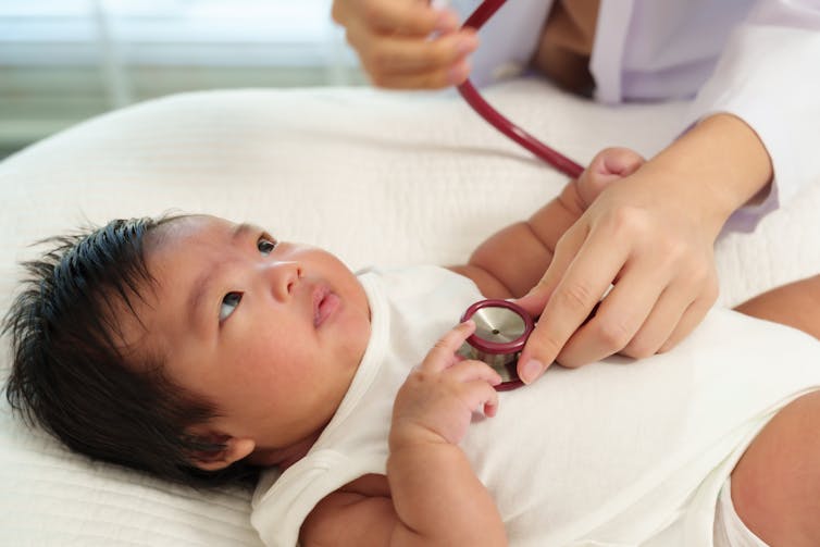 Newborn lying on exam table touching doctor's stethoscope