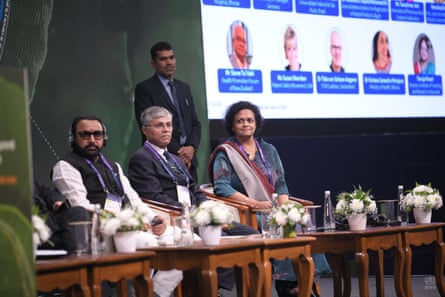 Three people in formal clothing stand behind desks in a conference hall