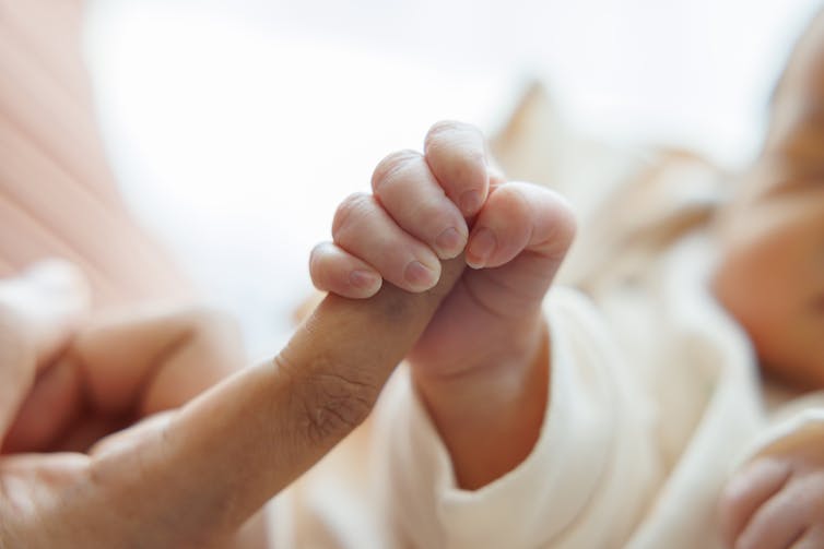 Newborn baby hand holding onto an adult finger.