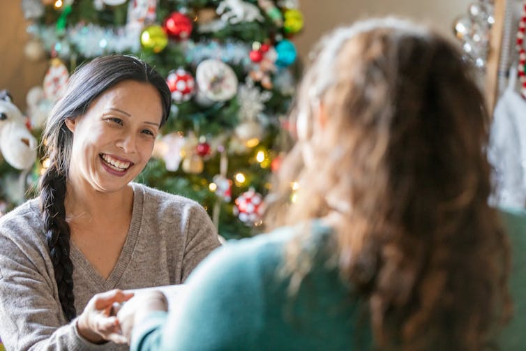 Woman standing in front of a Christmas tree receiving a gift