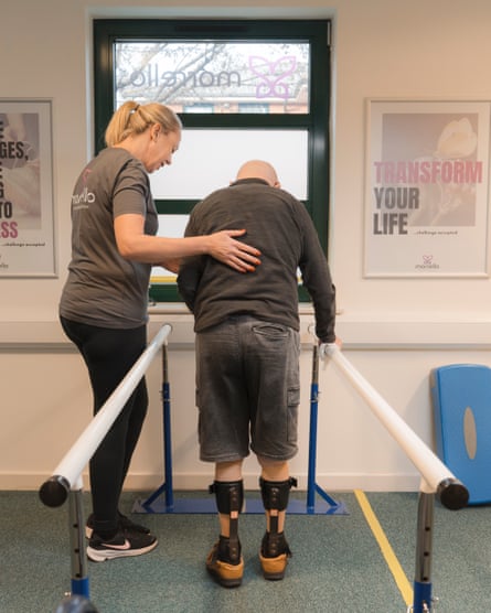 Harold Price pictured from behind being helped to use walking apparatus by a physiotherapist at a clinic
