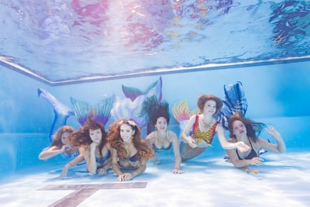 A pod of women dressed as mermaids underwater in a pool looking at camera