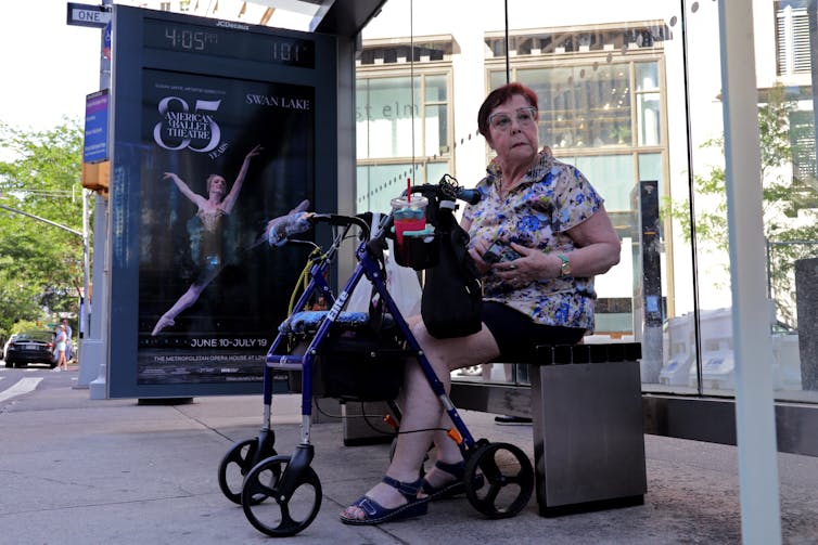 Woman with walker sits on bench under a bus shelter
