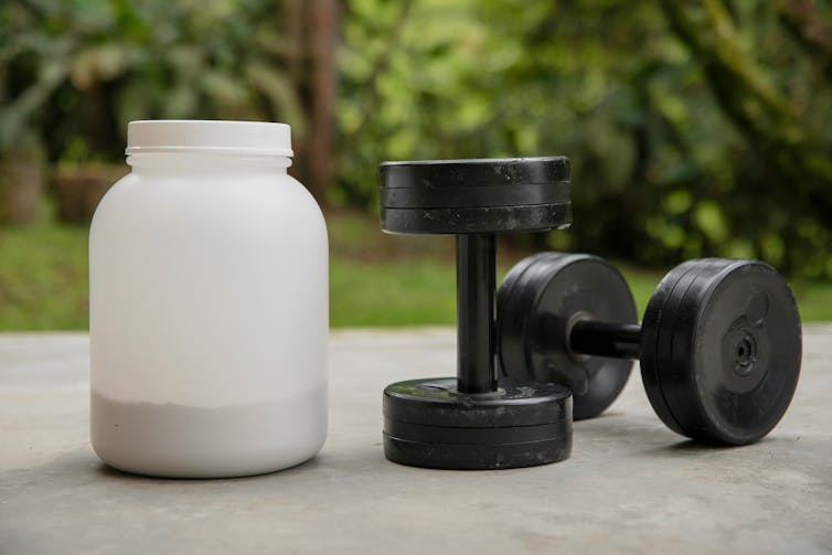 A plastic jar of powdered supplement and a pair of dumbbells