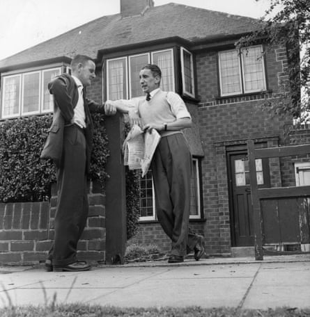 Two 1950s men in shirts, ties, jackets and knitted vests chat by the garden wall