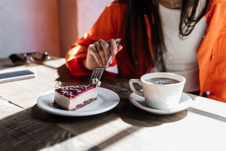 Woman in an orange jacket drinks eats cheesecake in a cafe