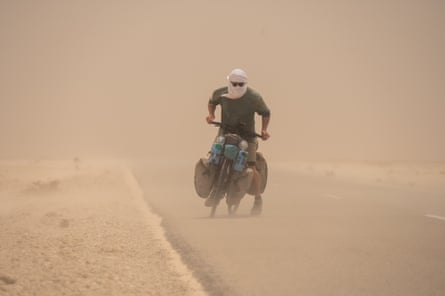 Graf, with a scarf around his face, struggles on his bike in a sandstorm