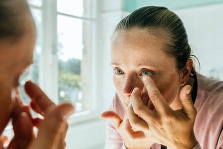 Woman putting in contact lens in bathroom while looking into a mirror