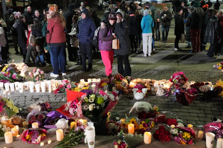 a group of people stand before a vigil with bouquets of flowers and lit candles.