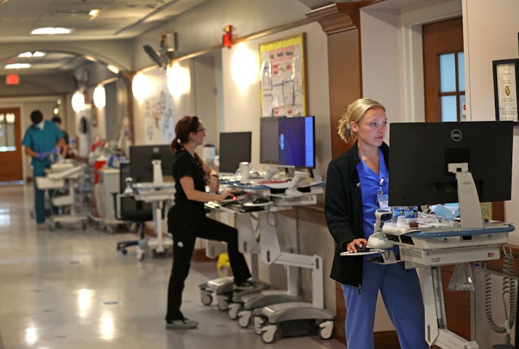 Three nurses work on patient charts outside patient rooms in a hospital.