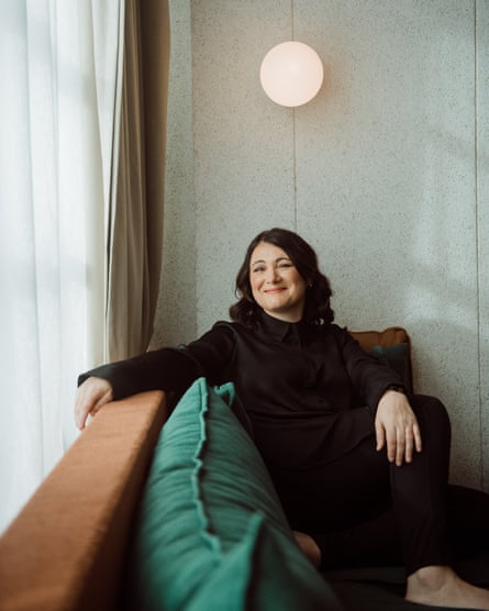 Radio broadcaster and comedian Jess McGuire sitting on a green couch underneath a round light fixture.