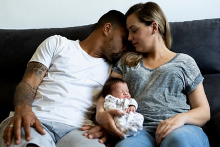 A couple holding a newborn baby sat on a sofa