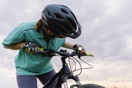 This image shows a woman wearing a helmet and adjusting the light on a bicycle