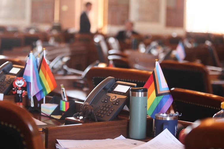 Small LGBTQ+ and trans pride flags adorn two legislators' desks