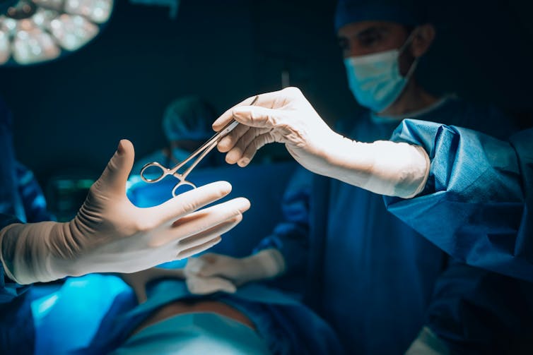A surgeon passes surgical scissors to a colleague during an operation