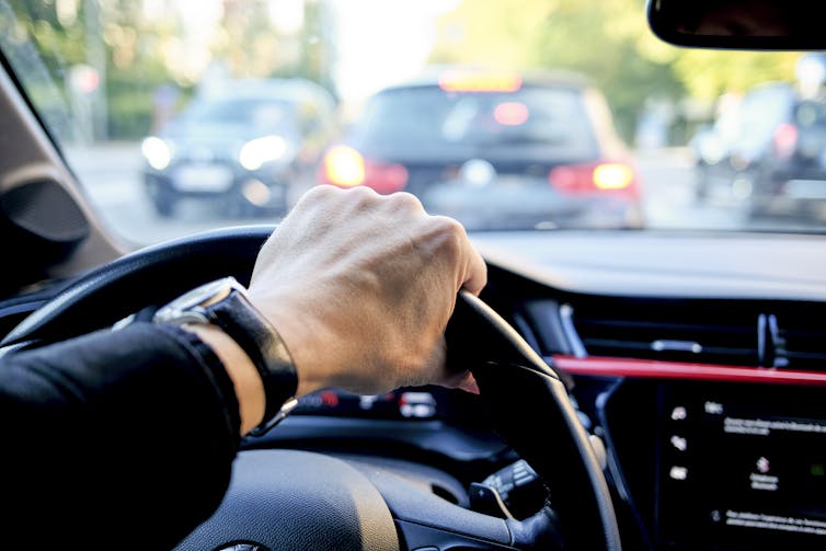 A driver's hand tightly grips a steering wheel with traffic visible ahead.