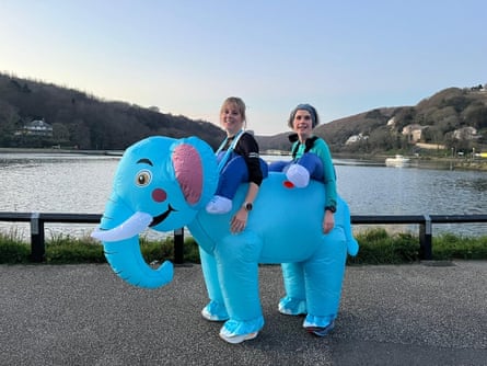 Two women sitting on a big blue inflatable elephant with a lake behind them