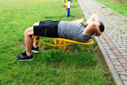 A man doing neck flexor exercises on a yellow workout platform in a park.