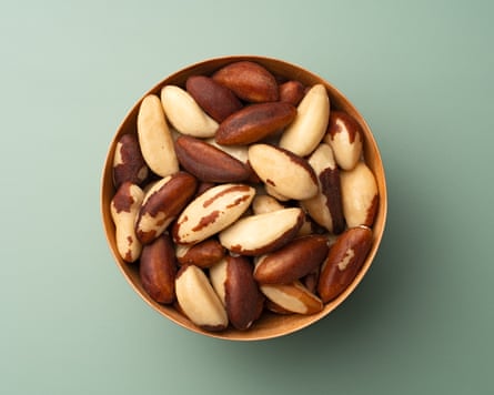 Brazil nuts in a bowl against a green background.