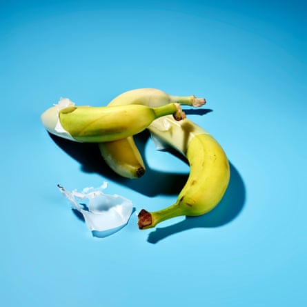 Three bananas in a messy pile with waxy covering peeling off then, against a sky-blue background