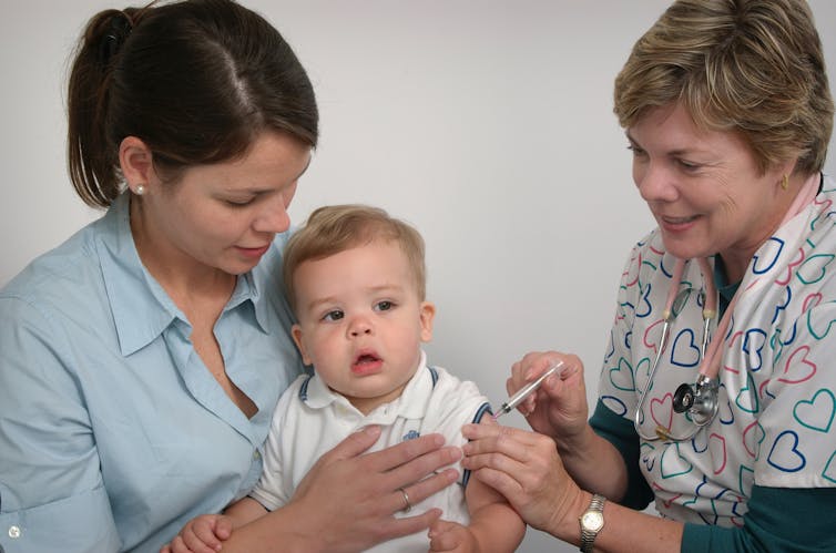 A female doctor gives a vaccine to a baby sitting in his mother's lap.
