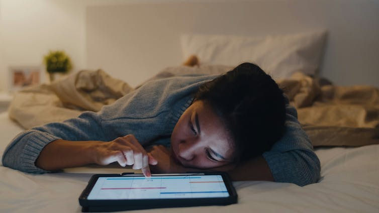 A woman on her bed alone scrolling through her iPad.
