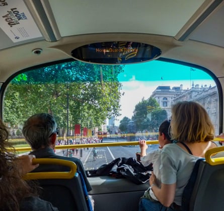 A family sits at the front of the upper deck of a double decker bus looking out the window at London