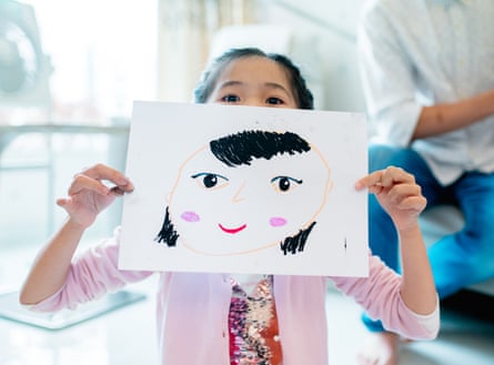 Young girl holding a self drawn portrait in front of her face