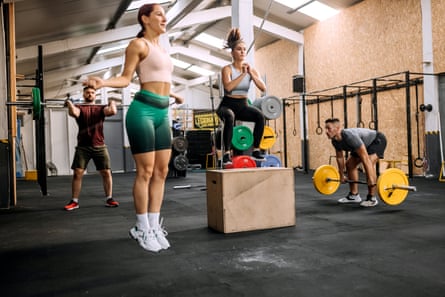 A group of people in a gym lifting weights, skipping and jumping on to a box