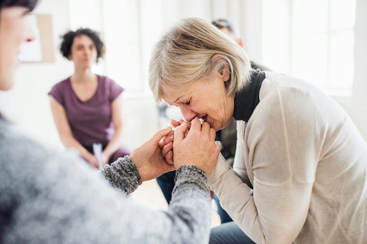 A woman in tears holds the hands of a loved one