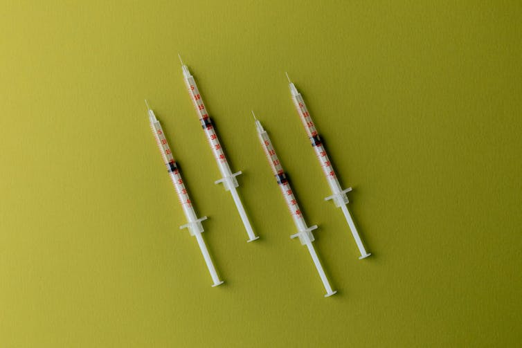 Four syringes against a yellow background