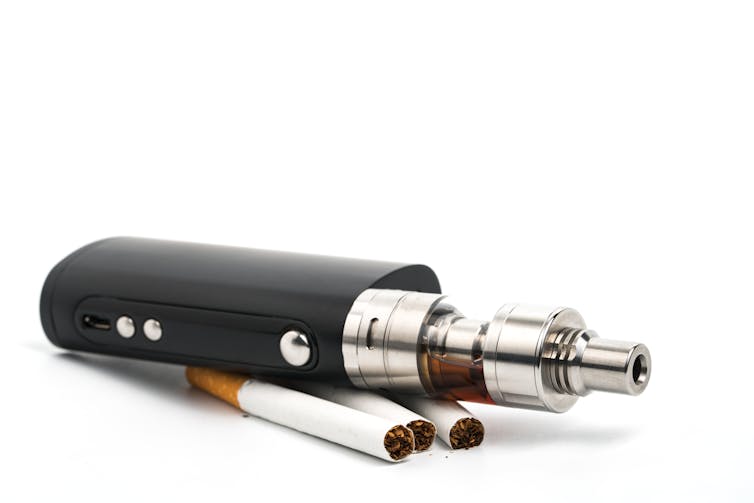 Large vape cartridge sitting atop three cigarettes