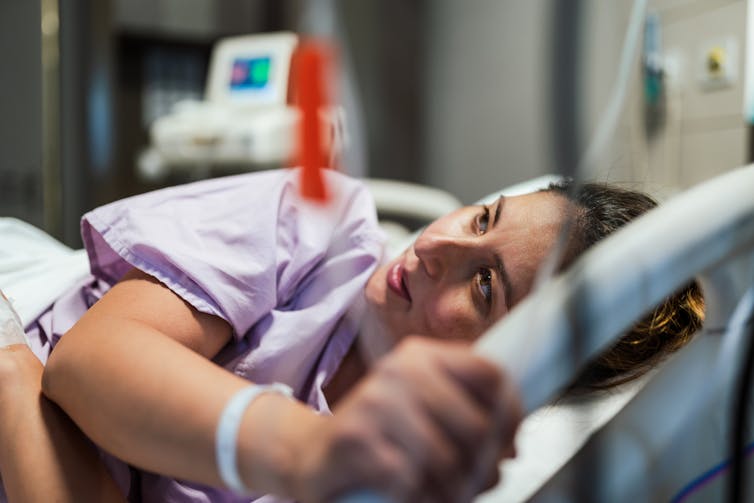 A white woman lies on her side in a hospital bed.