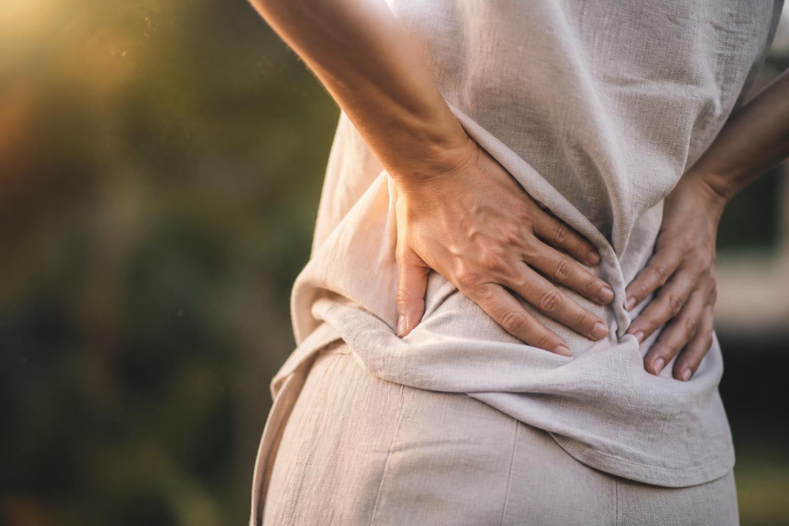 Close-up of hands gently holding a person's lower back, symbolizing relief from chronic pain in a natural setting.