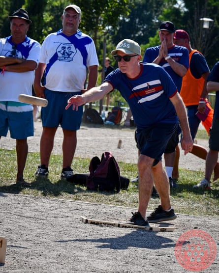 A man in a blue T-shirt and baseball cap throws a wooden skittle.