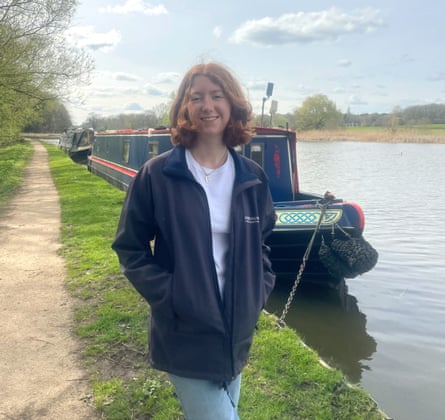 A woman stands on a canal towpath next to a canal boat