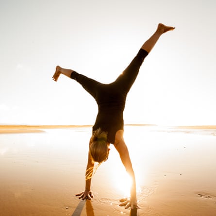 A woman doing a cartwheel while enjoying the sunset on a sandy beach