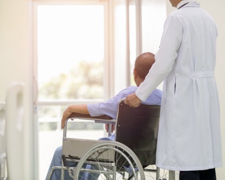 A person sitting in a wheelchair being pushed by a person in a white coat
