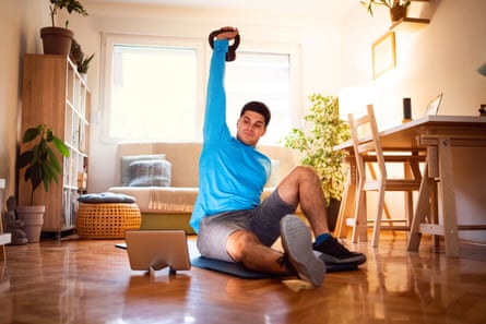 Young man exercising turkish get-up with a kettlebell, online workout on tabletYoung man at home following online turkish get-up exercise during quarantine.