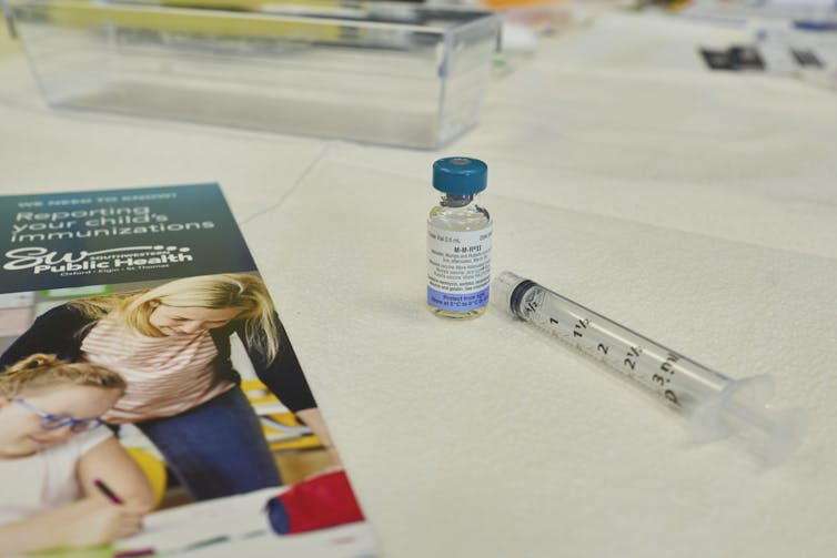 A vial of vaccine, a syringe and pamphlet on a white counter