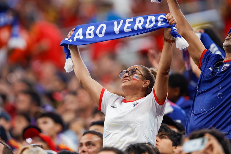 A woman hold a scarf reading 'Cabo Verde'.