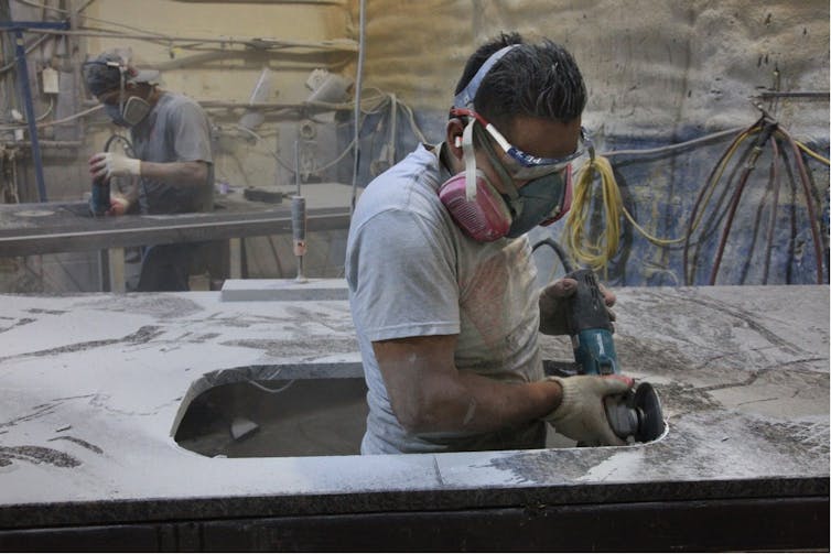Worker wearing dust mask and grinding a slab of engineered stone.