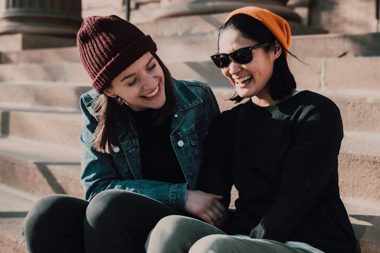 A couple sitting on stairs outdoors while one rests her hand on the other's arm.