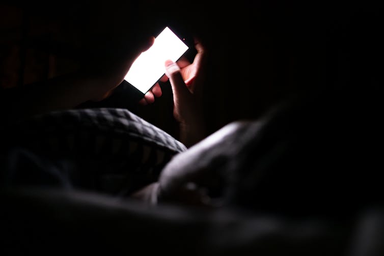 Person laying in bed looking at white glow of phone screen