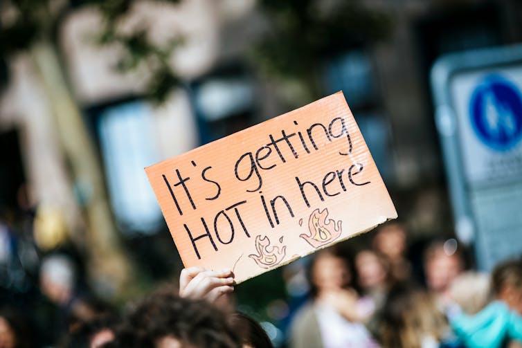 A hand holding up a sign reading 'It's getting hot in here'