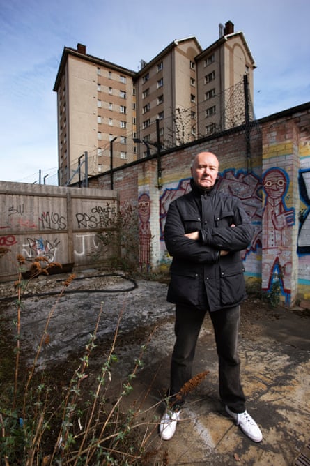 A man dressed in black with white trainers standing in front of a council estate